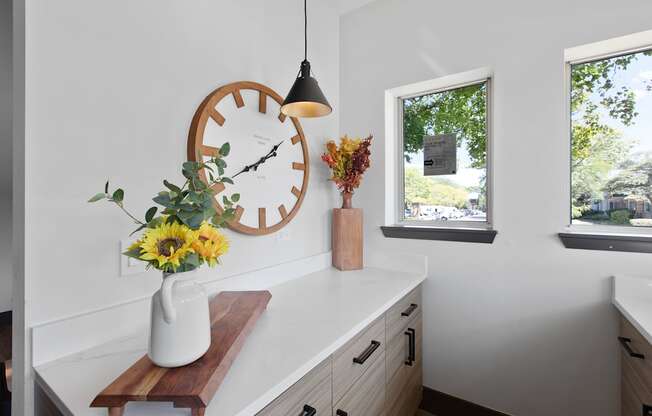 a kitchen counter with a clock and a vase of flowers