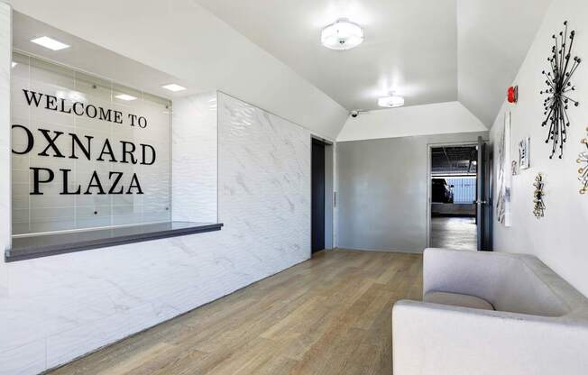 A white couch sits in a room with a sign that says "Welcome to Oxnard Plaza.".