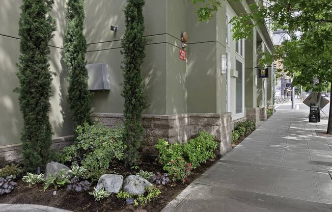 Sidewalk View of Stunning Landscaping  with tall Columns of Greenery and Delicate Flowers at Excalibur Apartment Homes, WA 98004