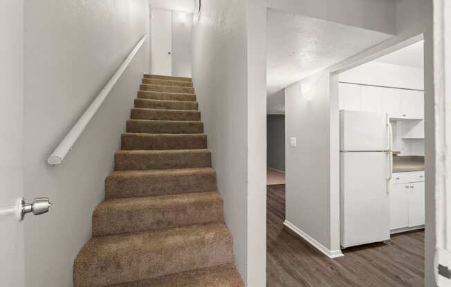 a staircase with carpeted stairs leading up to a kitchen with a refrigerator