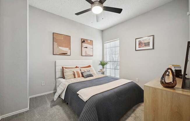 A bedroom with a bed, a ceiling fan, and a wooden nightstand.