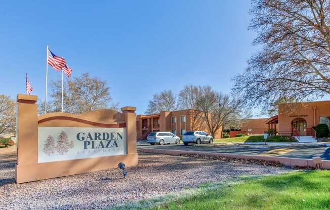 monument sign for Garden Plaza Apartments in front of a flag and parking lot