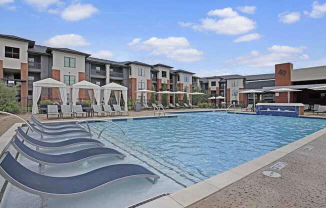 Modern 49 West Apartment complex with large outdoor pool and sun loungers. White cabanas line the poolside. Clear blue sky suggests a calm, sunny day.