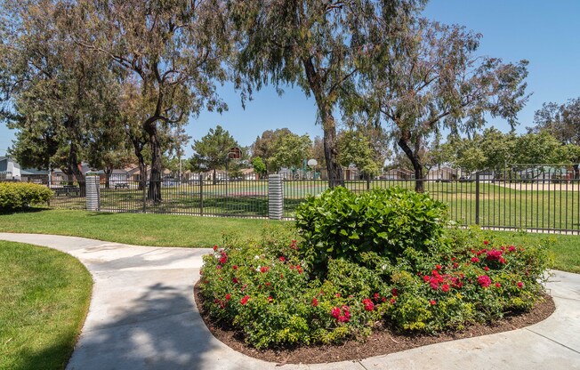 a park with a sidewalk and flowers and a fence