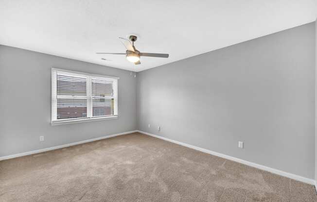 an empty bedroom with a ceiling fan and a window