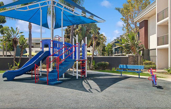 Community Playground with Slide and Blue Canopy at Madison Park Apartments located in Anaheim, CA.