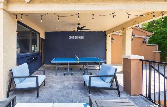 A pool table with a sign that says "Game On" is surrounded by chairs.