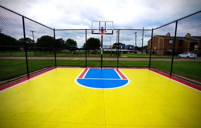 a yellow and blue basketball court with a red brick building in the background