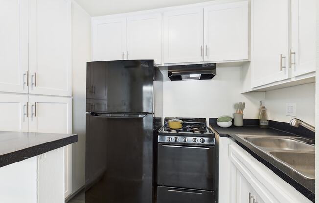 A black refrigerator and oven in a kitchen with white cabinets.