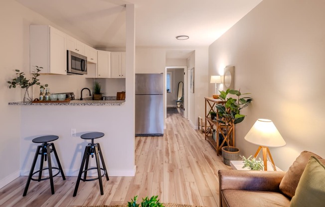 a living room with stools and a kitchen with a refrigerator