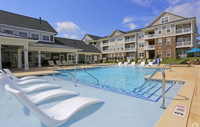 a swimming pool with white chairs in front of an apartment building