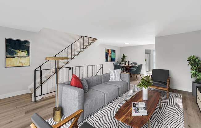 A living room with a grey couch, a coffee table, and a staircase.
