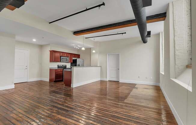 A room with wooden floors and a kitchenette in the corner.