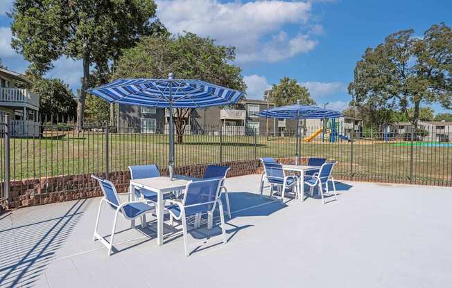 Poolside seating with blue and white striped umbrellas shading tables and chairs at Maplewood apartments in Shreveport, LA.