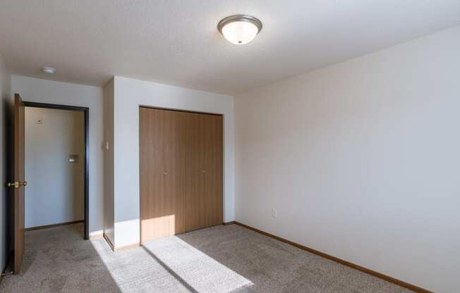 a bedroom with white walls and a door to a closet. Fargo, ND Eagle Run Apartments