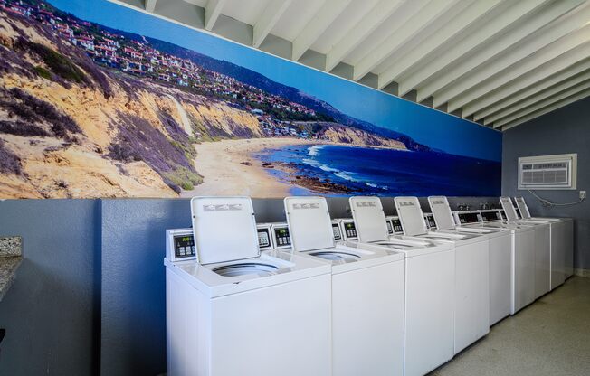 A row of washing machines in front of a wall mural.