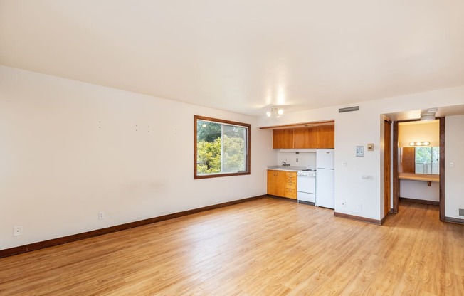 the living room and kitchen of an empty house with wood floors and a window