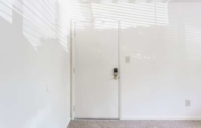 A white door with a black handle and lock in a white room