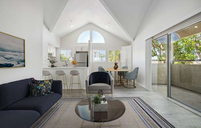 a living room with a couch and a coffee table in front of a kitchen with a breakfast