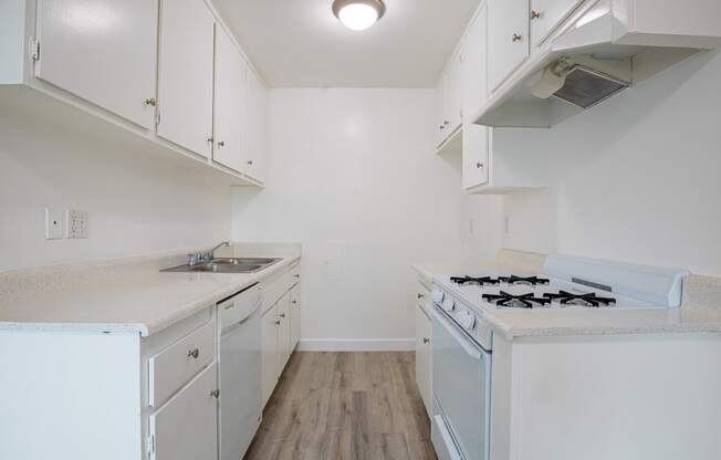 an empty kitchen with white cabinets and a stove and sink