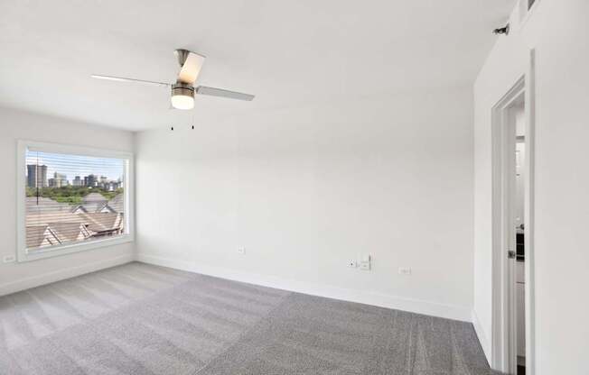 A room with a ceiling fan and a window overlooking a cityscape.