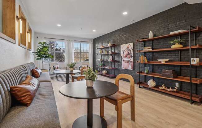 A living room with a grey sofa, a round table with a plant on it, and a wooden chair.