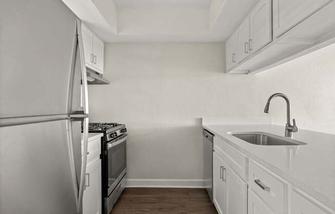 A white kitchen with a refrigerator, stove, and sink.