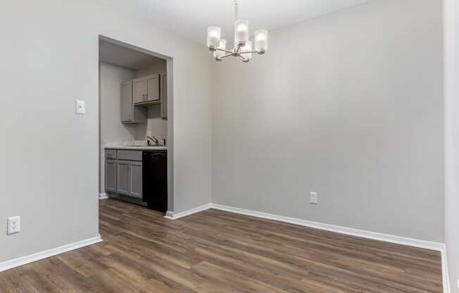 an empty living room with a kitchen in the background