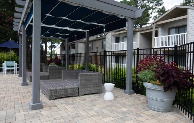 a pergola with a seating area and potted plants in front of an apartment complex