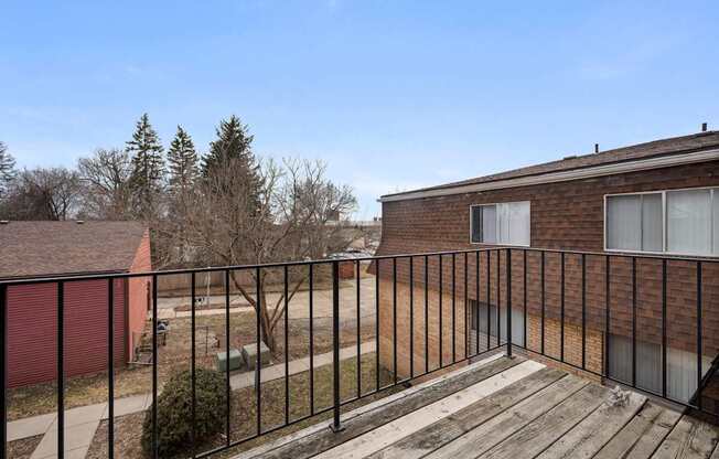A balcony with a black railing and a brick building in the background.
