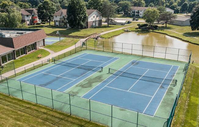 A tennis court with a green fence and a pond in the background.