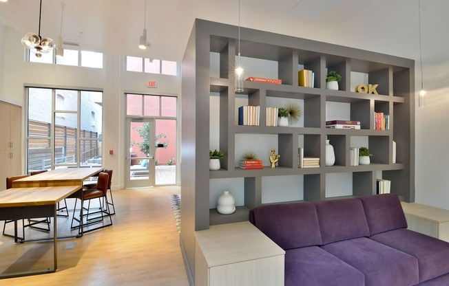 A modern living room with a purple couch and a grey bookshelf.