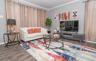 Model living room with a white couch, a glass coffee table, and a colorful rug at Maplewood apartments in Shreveport, LA.