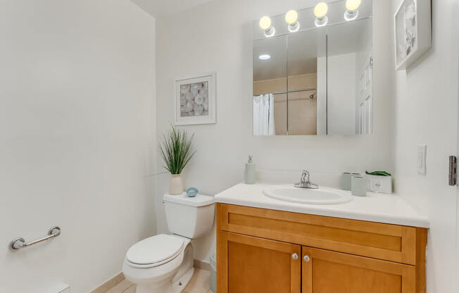 A bathroom with a white toilet, a wooden cabinet, and a mirror with lights above it.