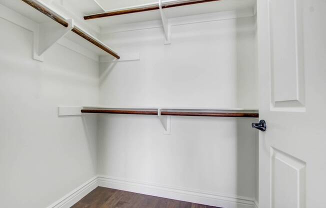 a walk in closet with white walls and a white closet door with a wood floor