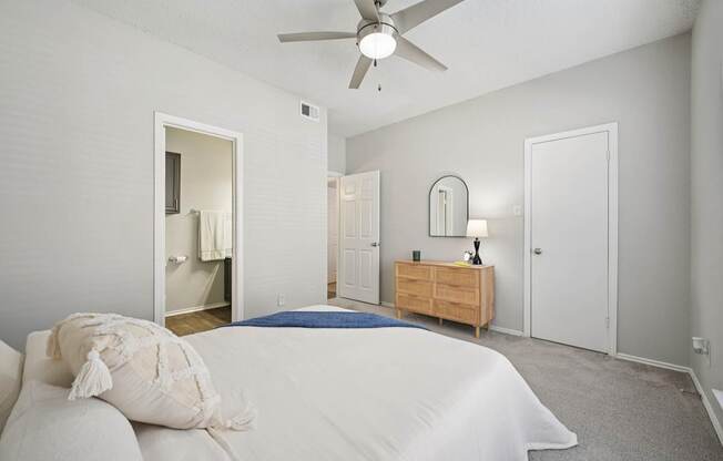 A bedroom with a bed, dresser, mirror, and a ceiling fan.