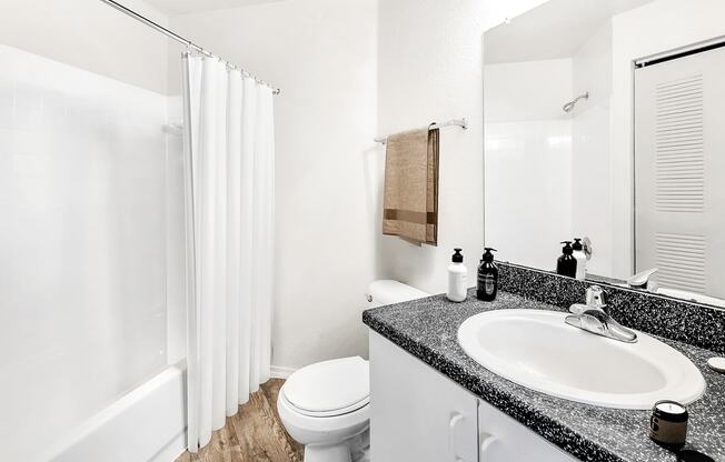 Virtually staged bathroom with large mirror, gray countertop, white cabinets and tiled tub with white shower curtain