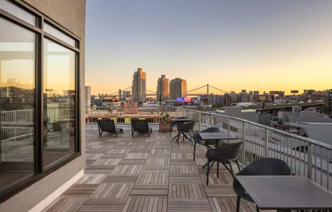 a balcony with tables and chairs overlooking a city at sunset