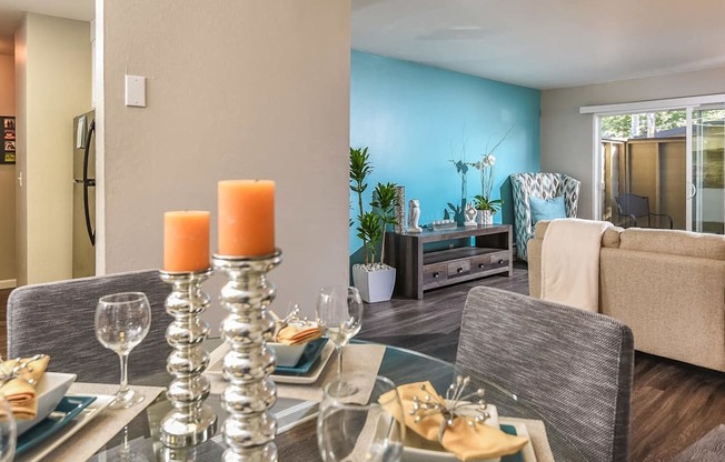 A dining table set with plates and glasses is in the foreground of a room with a blue wall and a couch in the background.