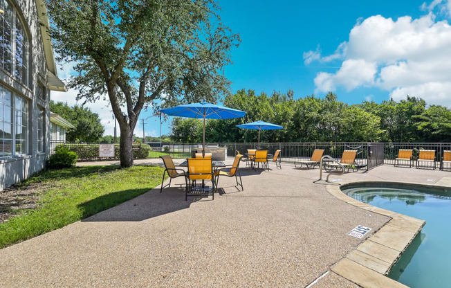 a patio with chairs and umbrellas next to a pool