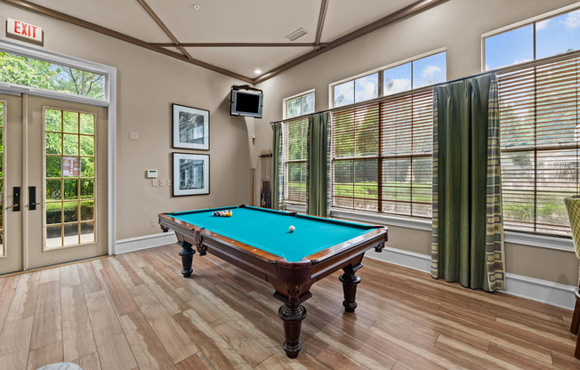 a pool table in club house with windows and a tv