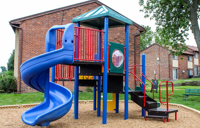 a playground with a blue slide in front of a brick building