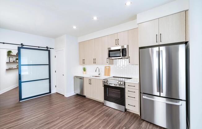 Kitchen with light wood cabinetry, quartz island seating, and stainless steel appliances arranged in a bright, open layout for daily cooking and gathering.