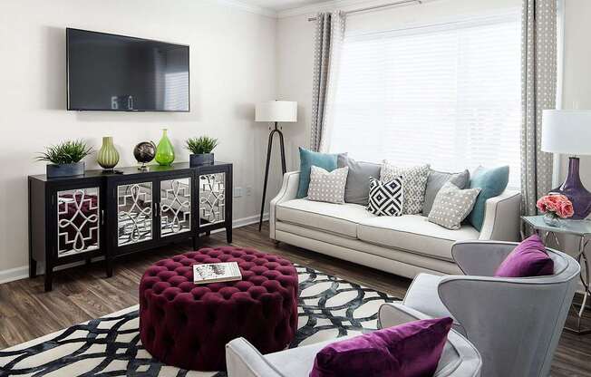 A living room with a white couch and a red ottoman.
