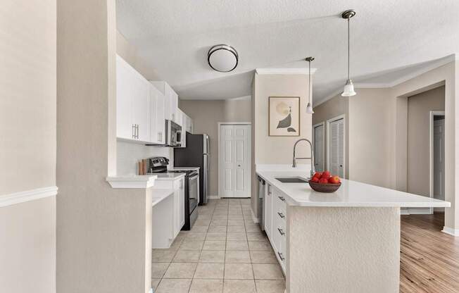 A kitchen with white cabinets and a white island with a bowl of strawberries on it.