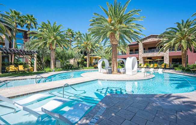 A pool surrounded by palm trees and a building in the background.