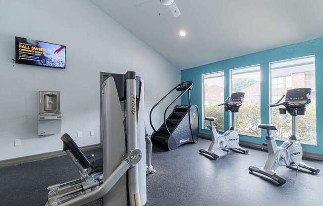 A gym with a row of stationary bikes and a treadmill.