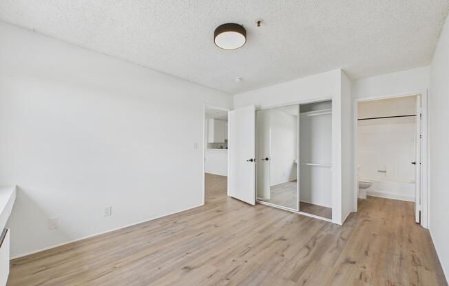 A room with white walls and wooden flooring with a ceiling light and a closet with a door open.