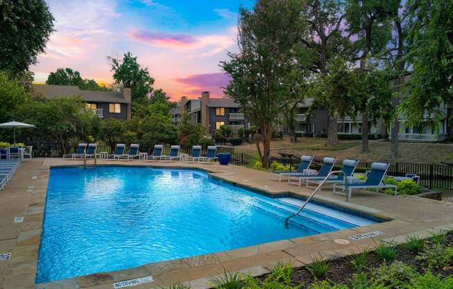 a resort style pool with blue chairs and a colorful sky