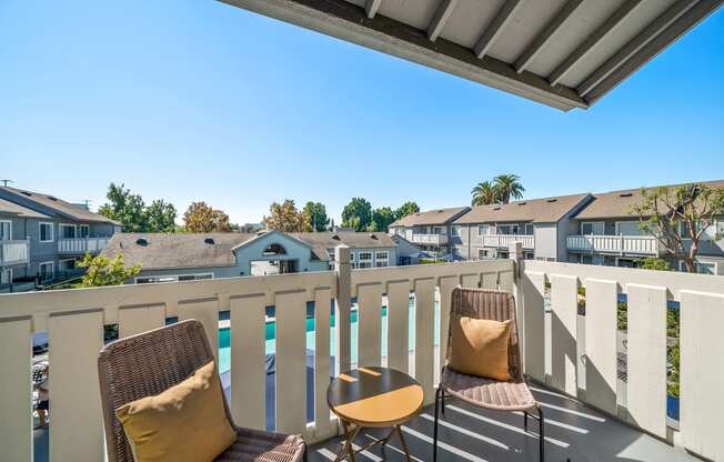 two chairs on a balcony overlooking a pool and houses